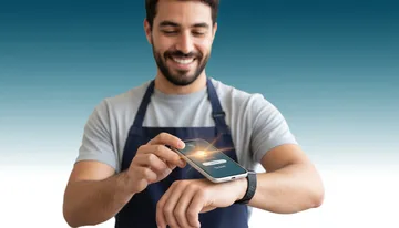 Smiling barista in an apron tapping a smartphone to the NFC band on his wrist